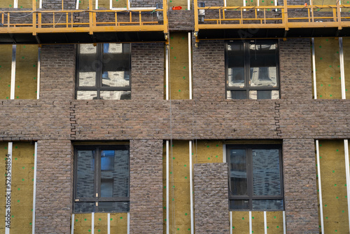 Process of installing exterior finishing coatings in form of brickwork on ventilated facade insulated with mineral wool walls of monolithic residential building. Suspended cradle platform for work