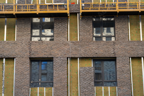Fotografie Process of installing exterior finishing coatings in form of brickwork on ventilated facade insulated with mineral wool walls of monolithic residential building