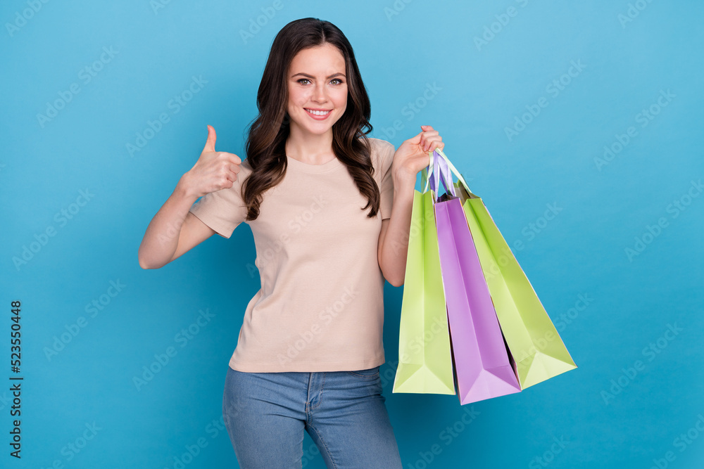 Photo of young beautiful female show thumb-up recommend fashion store shop isolated on blue color background Photo of young beautiful female show thumb-up recommend fashion store shop isolated on blue color background