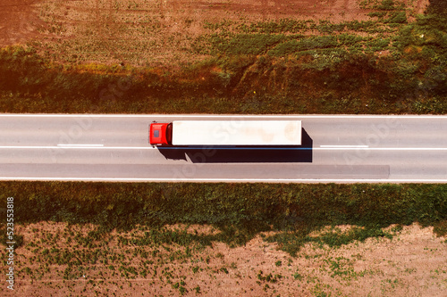 Aerial shot of semi-truck driving along the highway through countryside landscape, drone pov directly above. Transportation and logistics concept.