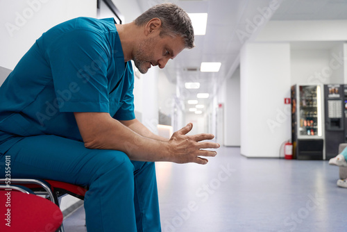 Upset doctor sitting on chair in hospital corridor