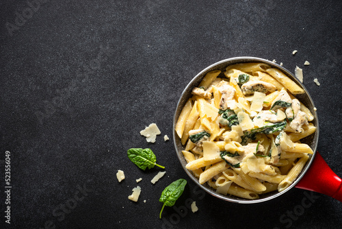 Pasta penne with chicken and spinach in creamy sauceon black table. Top view with copy space.