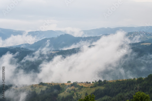 Amazing aerial view of beautiful low clouds creeping on the tree-covered mountain slopes, the Rhodopes in Bulgaria.