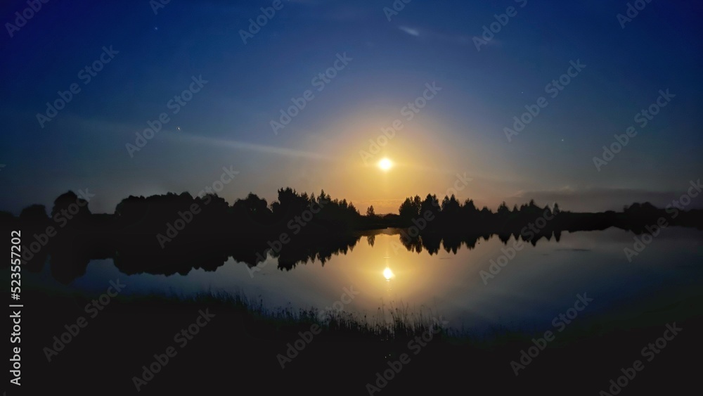 Reflection of Beautiful Full moon in water of a lake surrounded by trees