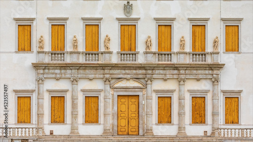 Numerose finestre di legno chiuse, statue e una porta su facciata di antico edificio storico in stile veneziano di colore bianco.