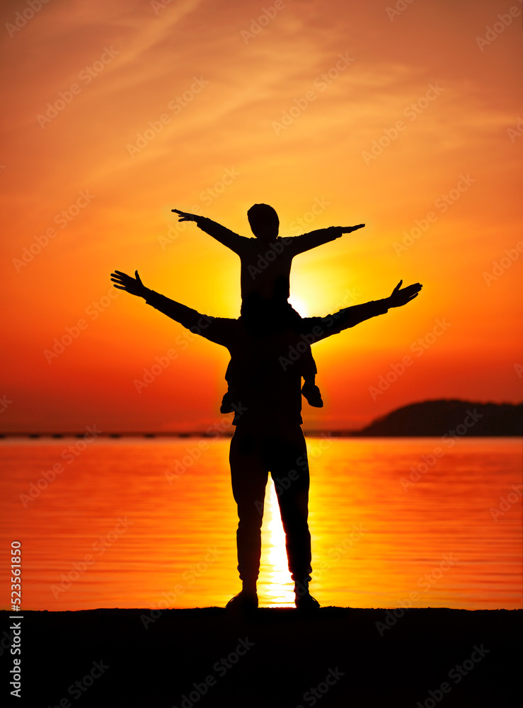 silhouette of a father with a child on his shoulders, arms outstretched at sunset