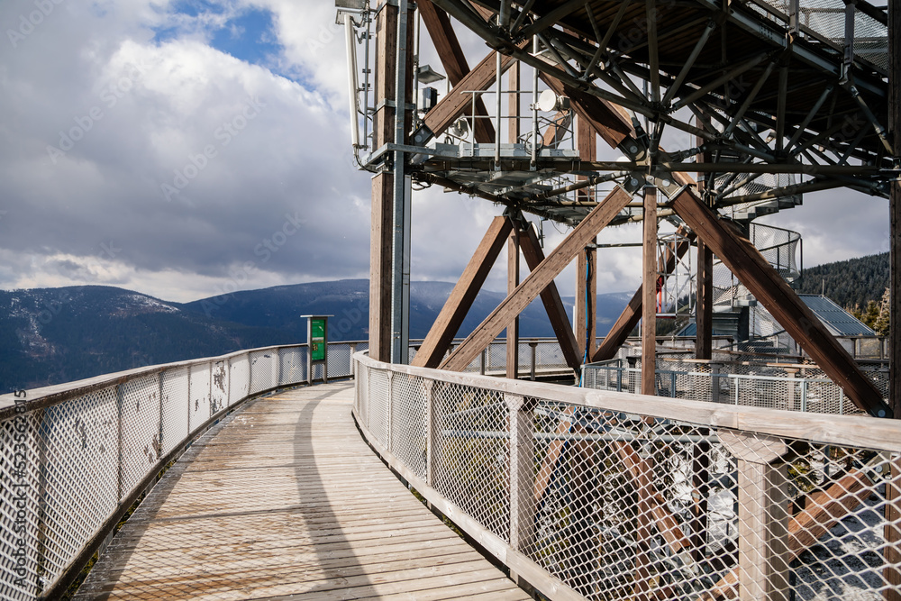 Fototapeta premium Dolni Morava, Czech Republic, 16 April 2022: Path in the clouds, tourist attraction with spiral platform to observation tower, landscape with forest and sky on mountains, Skywalk with snow