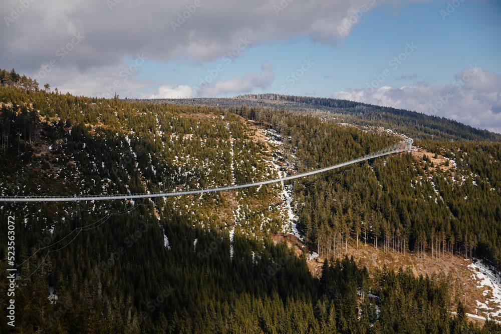 Obraz premium Dolni Morava, Czech Republic, 16 April 2022: Path in the clouds, largest suspension bridge in europe, landscape with forest and sky on mountains, Skywalk with snow, mountain lift, restaurant