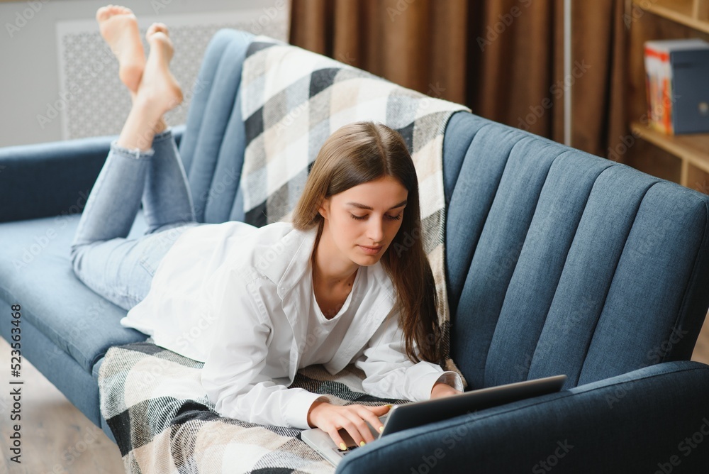 Freelancer working on laptop at home laying on comfortable beige sofa. Freelancer working on laptop at home laying on comfortable beige sofa.