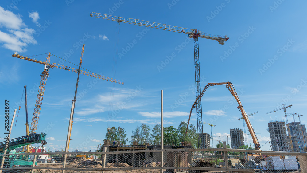 Construction of a multi-story residential buildings. Defocused foreground with young tree. Cranes work. Construction site. Construction of a multi-story residential buildings. Defocused foreground with young tree. Cranes work. Construction site.