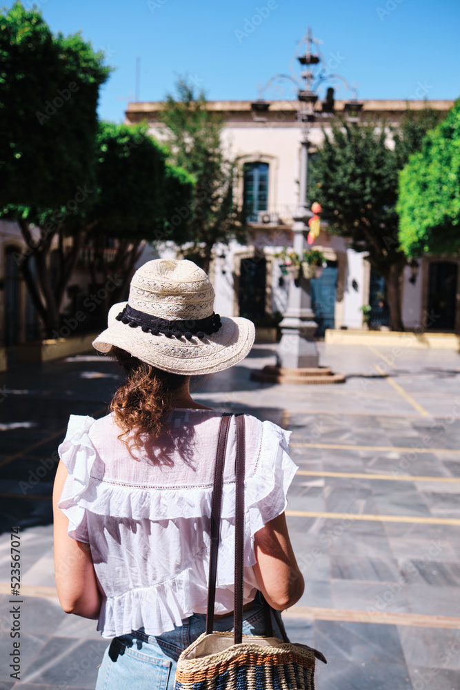 Tourist woman with hat on her back contemplating the main square of Níjar, Almería.