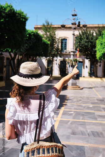Tourist woman with hat on her back looking at the main square of Níjar, Almería, and pointing with her finger.