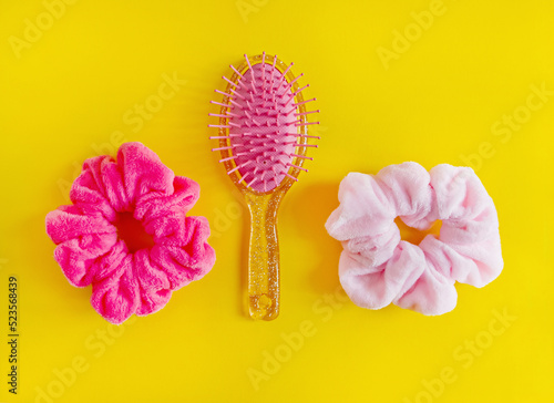 Pink Hair scrunchies and hairbrush on yellow background, beauty concept. flat lay with copy space for text photo