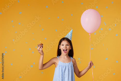 happy little birthday girl with party cone holding cupcake