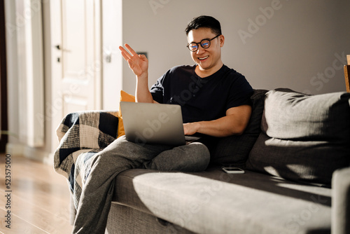 Adult brunette asian man smiling while using laptop at home © Drobot Dean