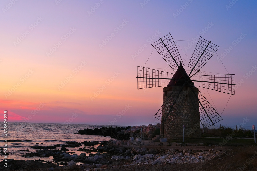 Windmill on the shore seaside with sunset in the background. North of Sicily, Trapani, old fashioned windmill on the coast.