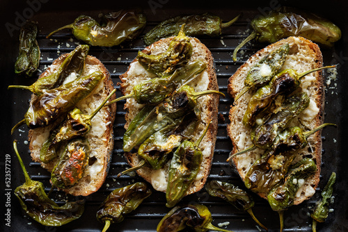 Grilled sandwiches made of traditional bread with the addition of green padron peppers and cheese on a grill plate, top view photo