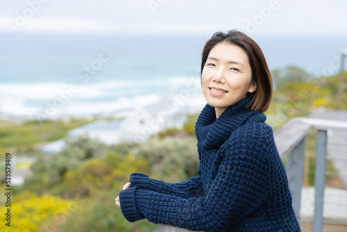 Portrait of happy asian woman wearing jumper and leaning on balcony alone