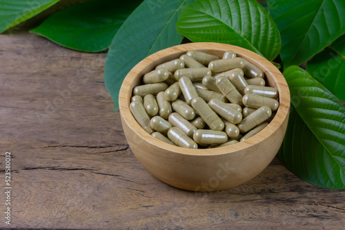 Mitragyna Speciosa Korth or kratom capsules in wooden bowl with green leaf on rustic wooden table.