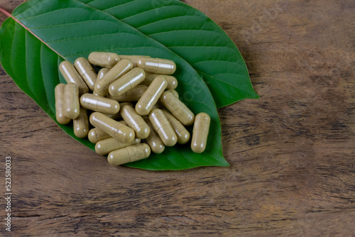 Mitragyna Speciosa Korth or kratom capsules with green leaf on rustic wooden table, top view.