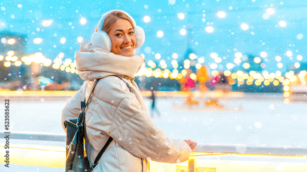 Wintertime. Christmas holiday evening, woman standing outside and smile. Christmas illumination and decoration background. Winter holiday season.