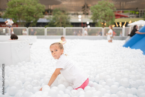 Happy little girl playing white plastic balls pool in amusement park. playground for kids. photo