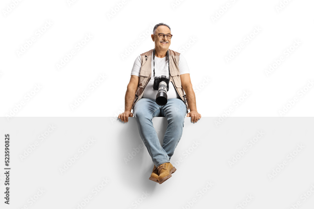 Photographer with a camera sitting on a blank panel and smiling at camera Photographer with a camera sitting on a blank panel and smiling at camera