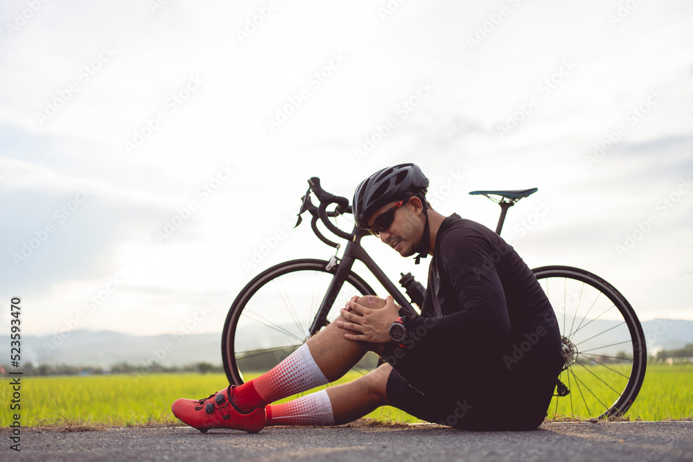 Obraz premium Bike injuries. Man cyclist fell fell off road bike while cycling. Bicycle accident, injured knee. Road in Thailand.