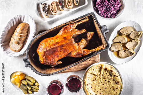 Foto Roast goose with side dishes, red cabbage, roast, strudel, potato dumplings, pickles, bread and red wine