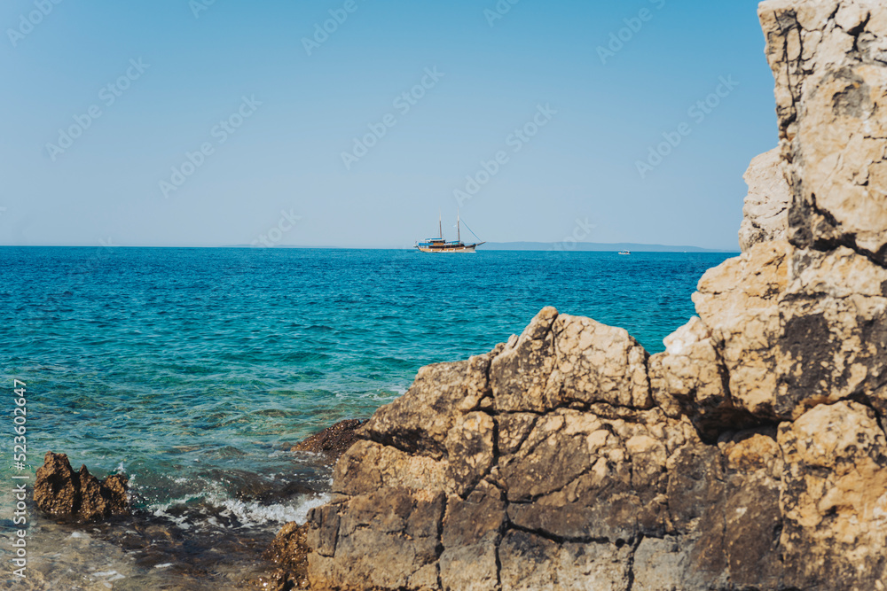 A ship on the turquoise sea behind the rocks. Summer landscape.