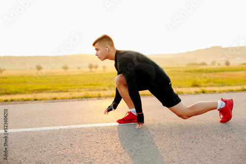 Fotografie Close-up of male crouch start on asphalt track outside and turning back to camera