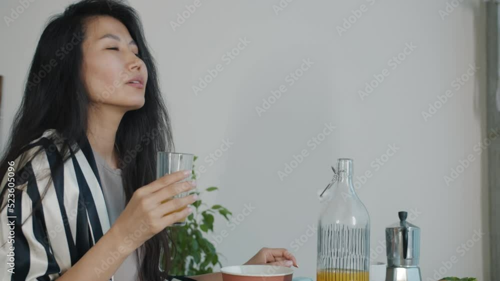 Cheerful Asian woman drinking fresh orange juice during breakfast at home smiling enjoying drink. People and healthy lifestyle concept. Cheerful Asian woman drinking fresh orange juice during breakfast at home smiling enjoying drink. People and healthy lifestyle concept.