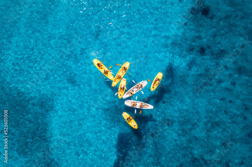 Aerial view of yellow kayaks in blue sea at sunset in summer. People on floating canoes in clear azure water. Sardinia island, Italy. Tropical landscape. Sup boards. Active travel. Top view from drone