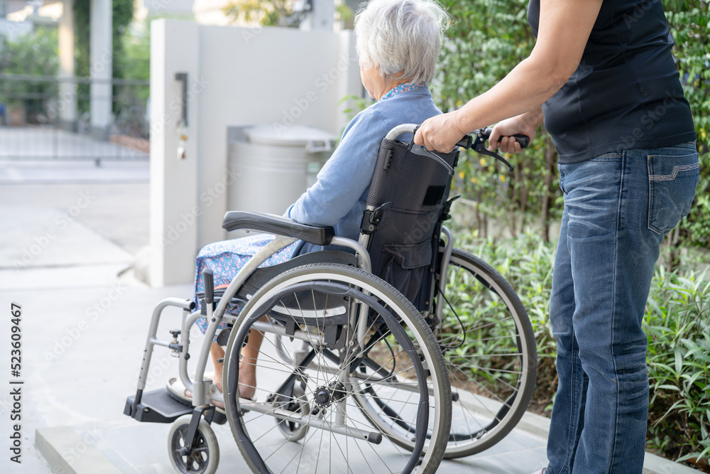 Caregiver help and care Asian senior or elderly old lady woman patient sitting on wheelchair at nursing hospital ward, healthy strong medical concept