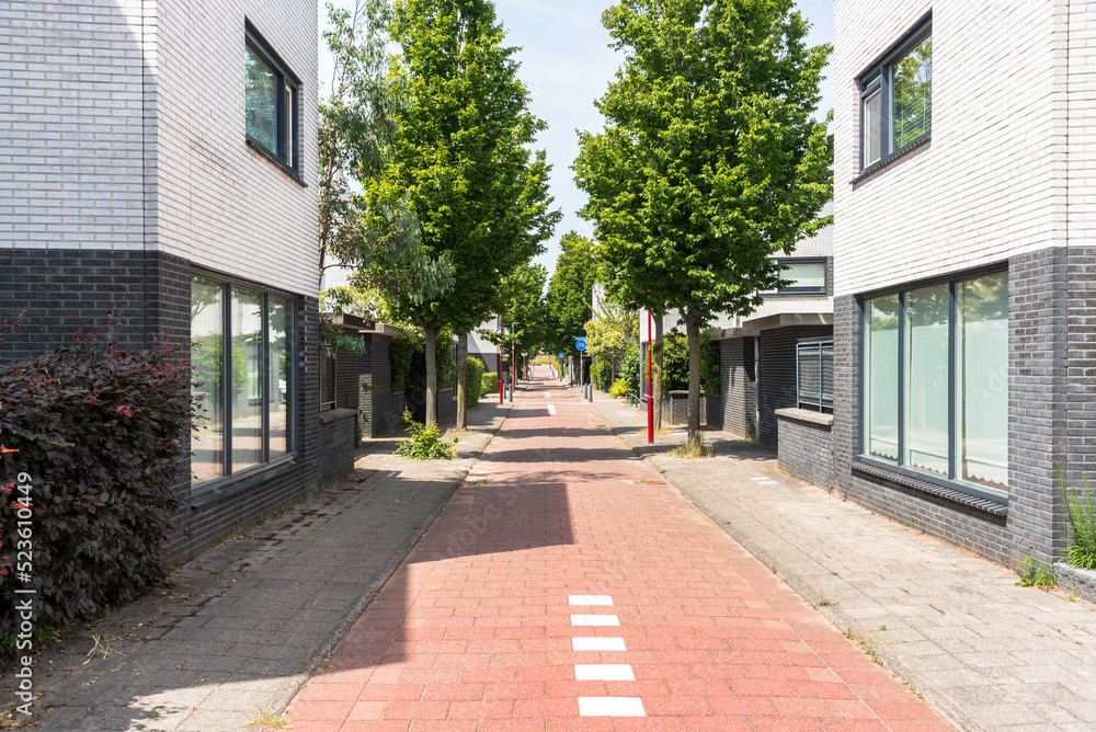 Deserted tree lined bicycle lane running between modern brick residential buildings on a sunny summer day