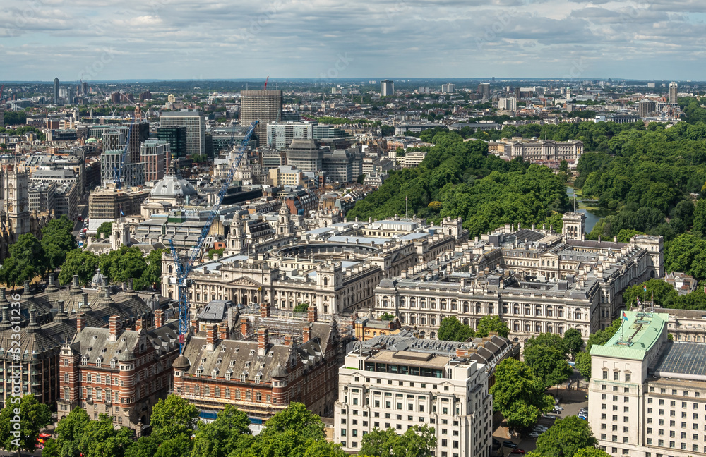 London, UK - July 4, 2022: Seen from London Eye. Imperial War Museum square buildings with green St. James's park behind set in dense urban jungle cityscape under blue cloudscape.