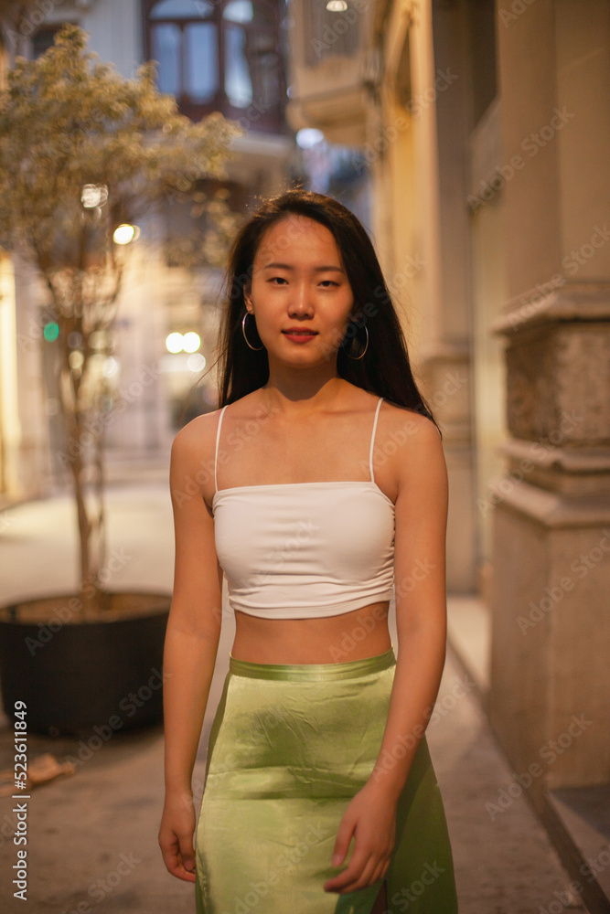 Young Asian girl tourist walking in the street of European town at night. Chinese student girl in Europe in summer clothes