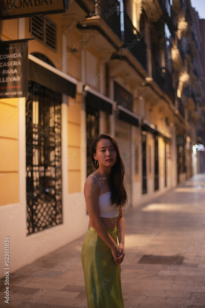 Young Asian girl tourist walking in the street of European town at night. Chinese student girl in Europe in summer clothes Young Asian girl tourist walking in the street of European town at night. Chinese student girl in Europe in summer clothes