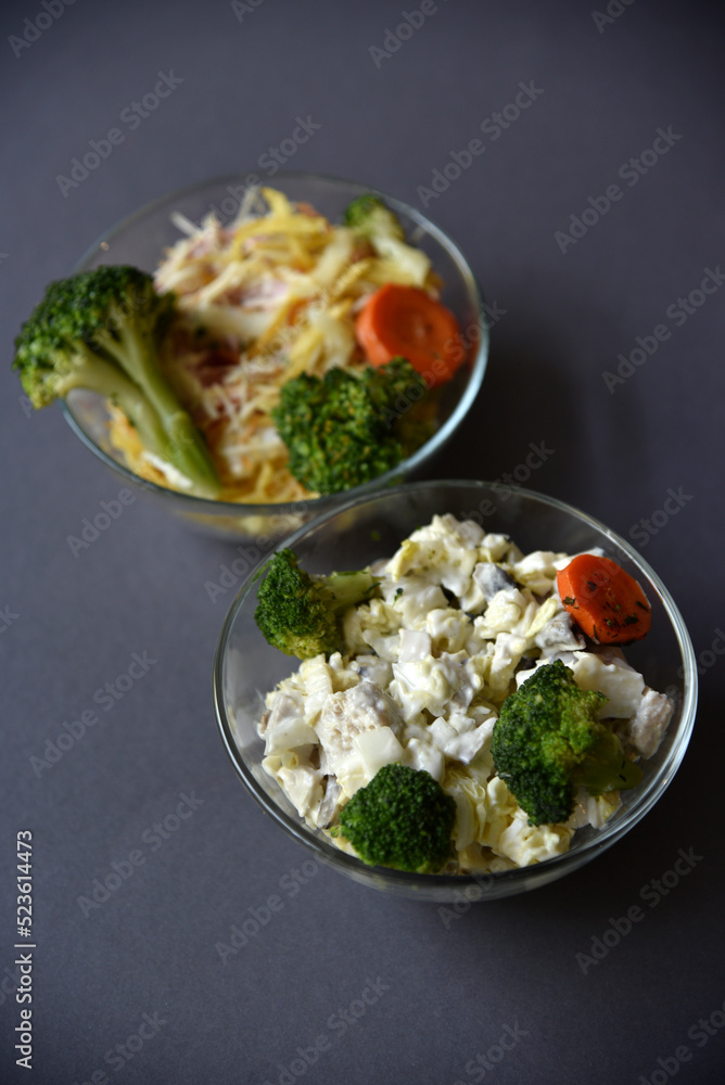 Salads with mayonnaise and vegetables with meat in glass salad bowls on a black background. Delicious salads with forks on a black background. Salads with a still life.