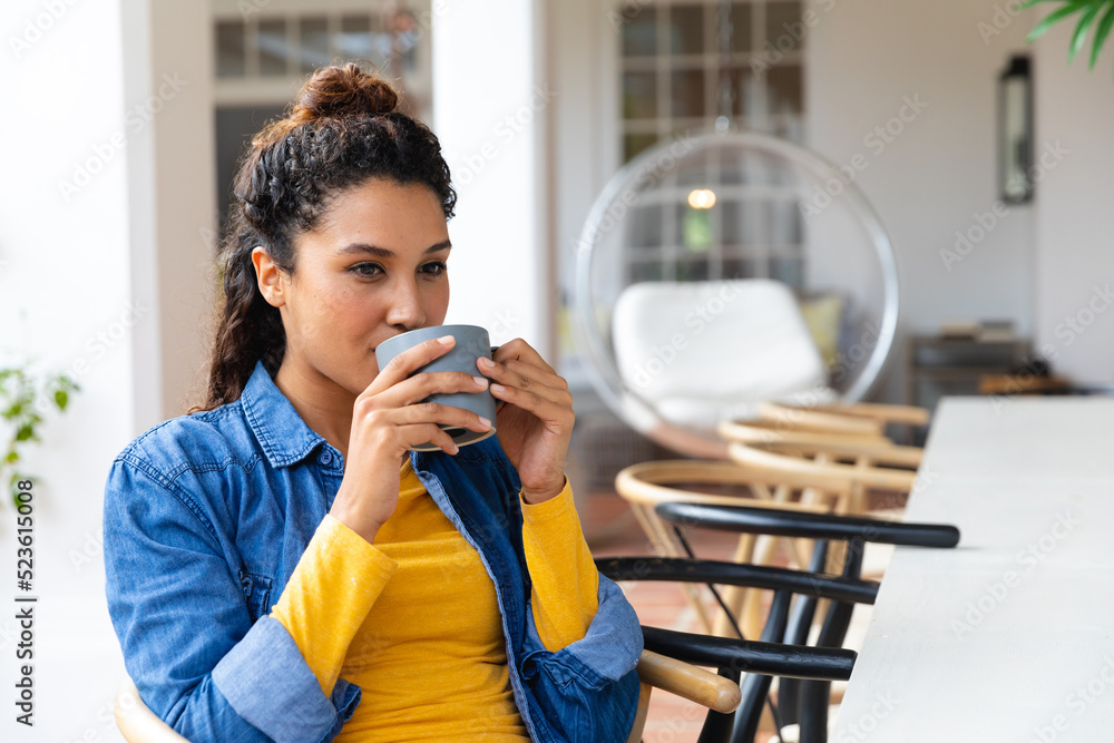 Happy biracial woman sitting on garden terrace drinking coffee outside house