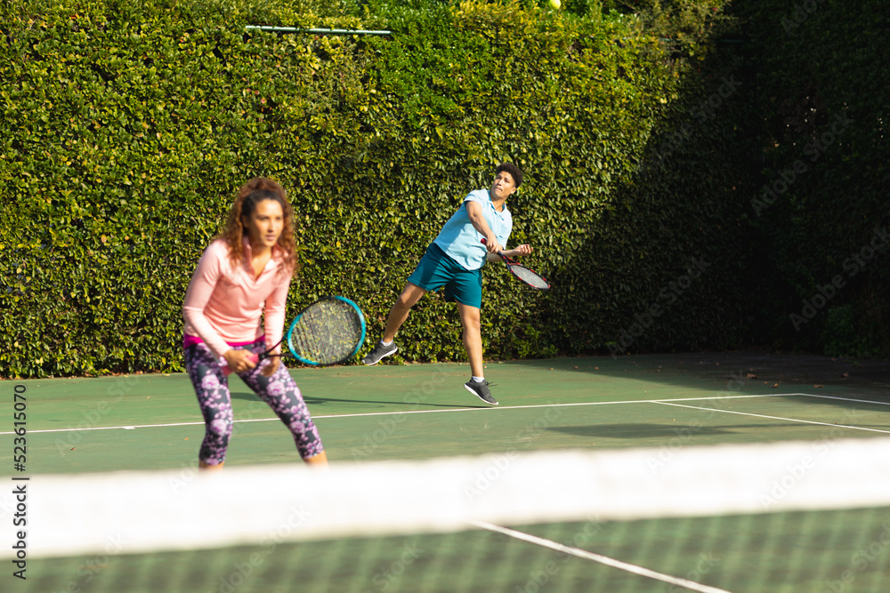Obraz premium Biracial couple playing tennis on sunny outdoor tennis court