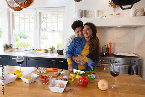 Happy biracial couple preparing food and embracing in kitchen