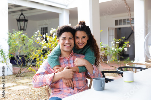 Portrait of happy biracial couple on garden terrace embracing outside house smiling