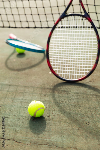 Detail of two tennis rackets and balls by the net at an outdoor tennis court, selective focus