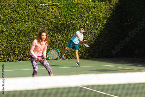 Biracial couple playing tennis on sunny outdoor tennis court