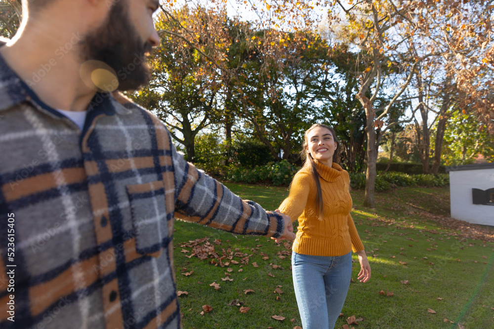 Fototapeta premium Happy caucasian couple holding hands walking in sunny autumn garden