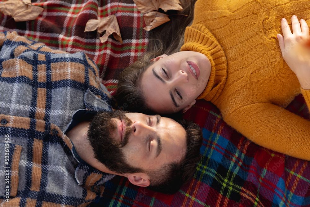 Fototapeta premium Image of happy caucasian couple lying on blanket in autumn garden