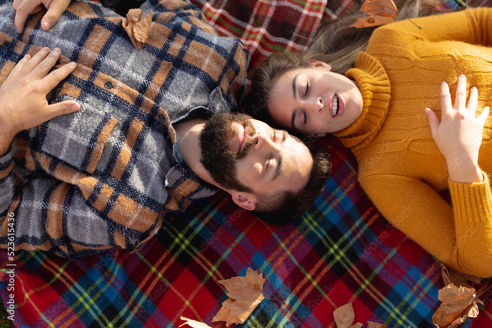 Fototapeta premium Image of happy caucasian couple lying on blanket in autumn garden
