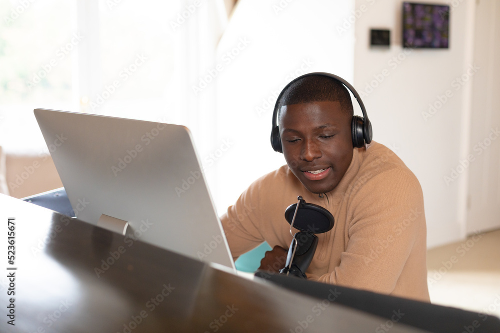 Smiling african american man in headphones making podcast at home using computer and microphone Smiling african american man in headphones making podcast at home using computer and microphone
