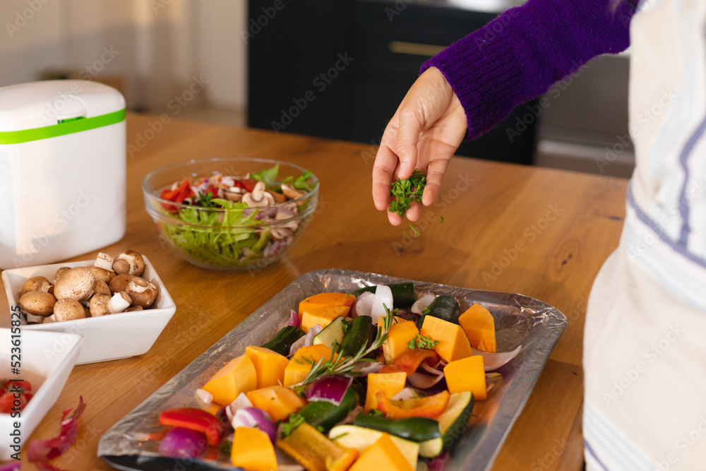 Midsection of caucasian woman standing in kitchen sprinkling fresh herbs on chopped vegetables Midsection of caucasian woman standing in kitchen sprinkling fresh herbs on chopped vegetables